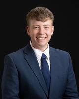 Man in a blue suit and tie smiling against a black background.