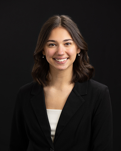 Smiling woman in a black blazer against a black background.