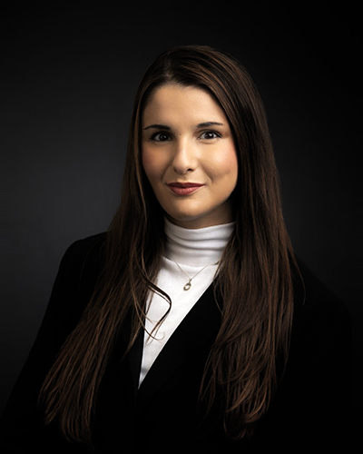 Professional woman in a black blazer and white turtleneck, set against a dark background.