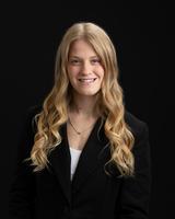 Smiling woman with long wavy blonde hair wearing a black blazer, set against a dark background.