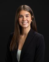 Smiling woman in a dark blazer against a black background.
