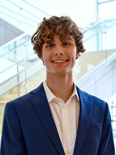 Smiling person in a blue suit standing in front of a modern staircase.