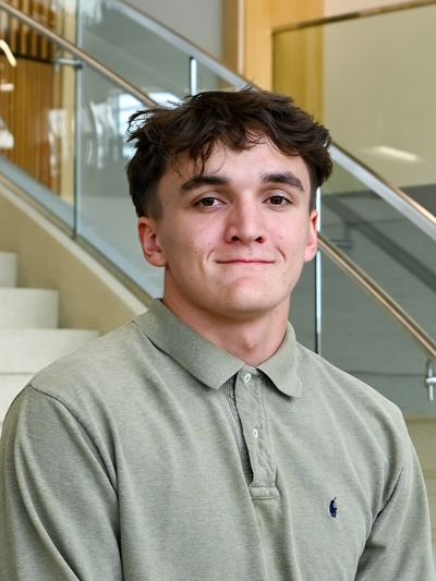 Man with short brown hair wearing a green polo stands near stairs indoors.