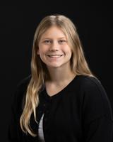 Smiling woman with long blonde hair wearing a black cardigan, posed against a dark background.