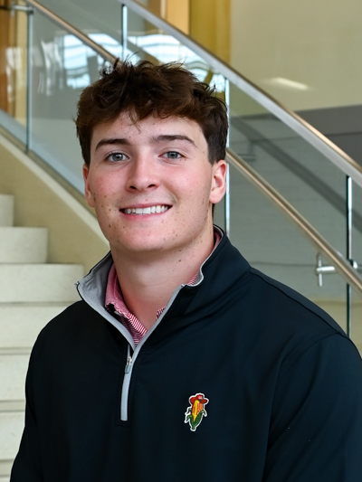 Smiling person wearing a black pullover with embroidered logo, standing near stair railing indoors.
