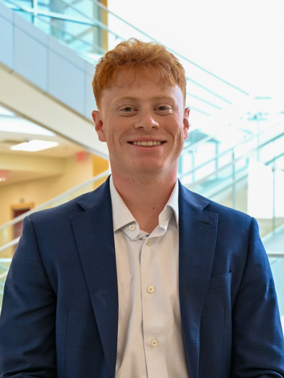 Professional man in a blue suit smiling in a bright indoor setting with modern stairs.