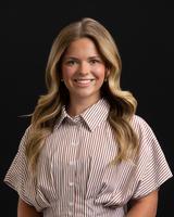 A woman with wavy blonde hair wearing a striped blouse, smiling against a black background.
