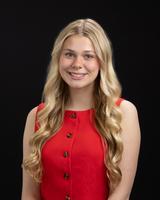 Smiling woman with long blonde hair wearing a red dress, standing against a black background.