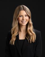 Smiling woman with long blonde hair in a black blazer, posed against a dark background.