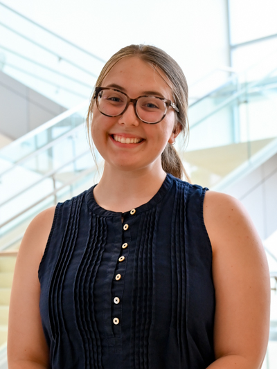 Smiling woman with glasses and a navy blouse standing near modern stairs indoors.