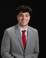 Man in a gray suit with a red tie, smiling against a black background.