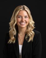 Smiling woman with wavy blonde hair, wearing a black blazer against a dark background.