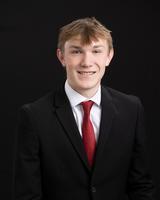 Young man in a suit and red tie, smiling against a black background.