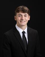 Man in a black suit and tie smiling against a black background.