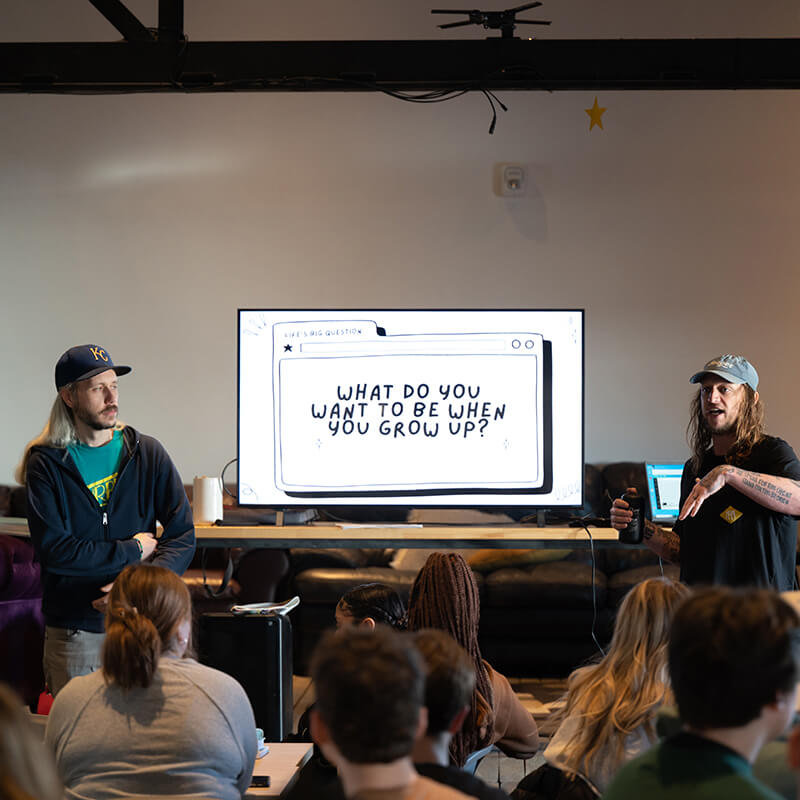 Two long-haired men give presentation to students.