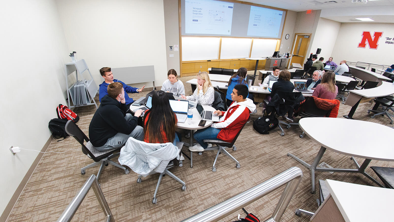 Students sitting at tables in small groups discuss marketing.