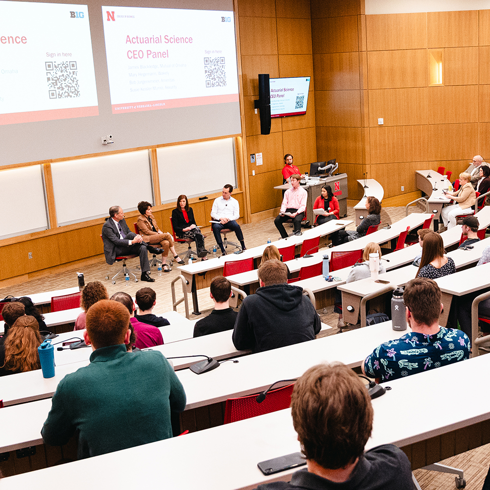 Panel discussion in a lecture hall with seated audience and speakers in business attire.