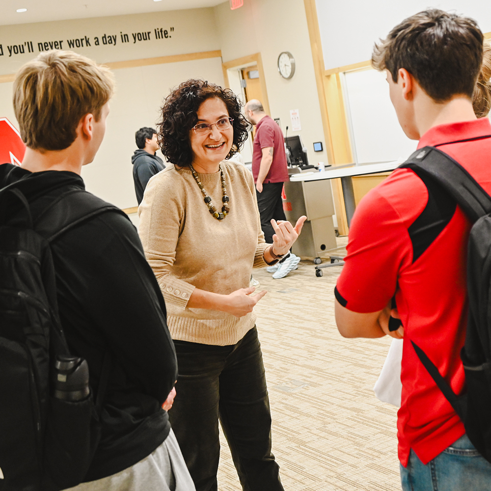 Woman interacting with three students in a classroom setting.