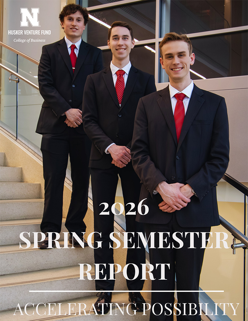 Three men in suits and red ties pose on a staircase inside a modern building.