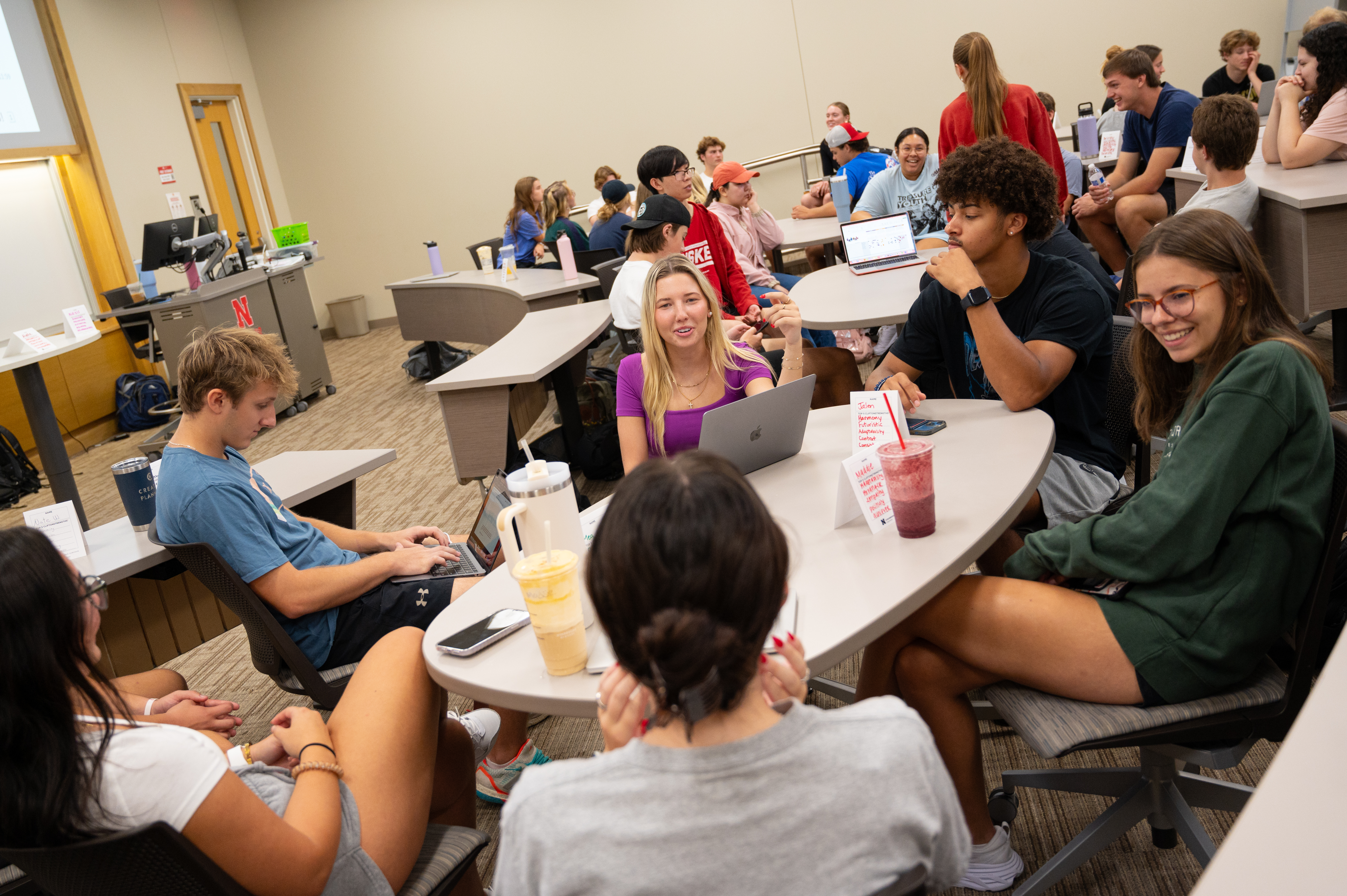 Students sitting at tables in a classroom, engaged in group discussions.