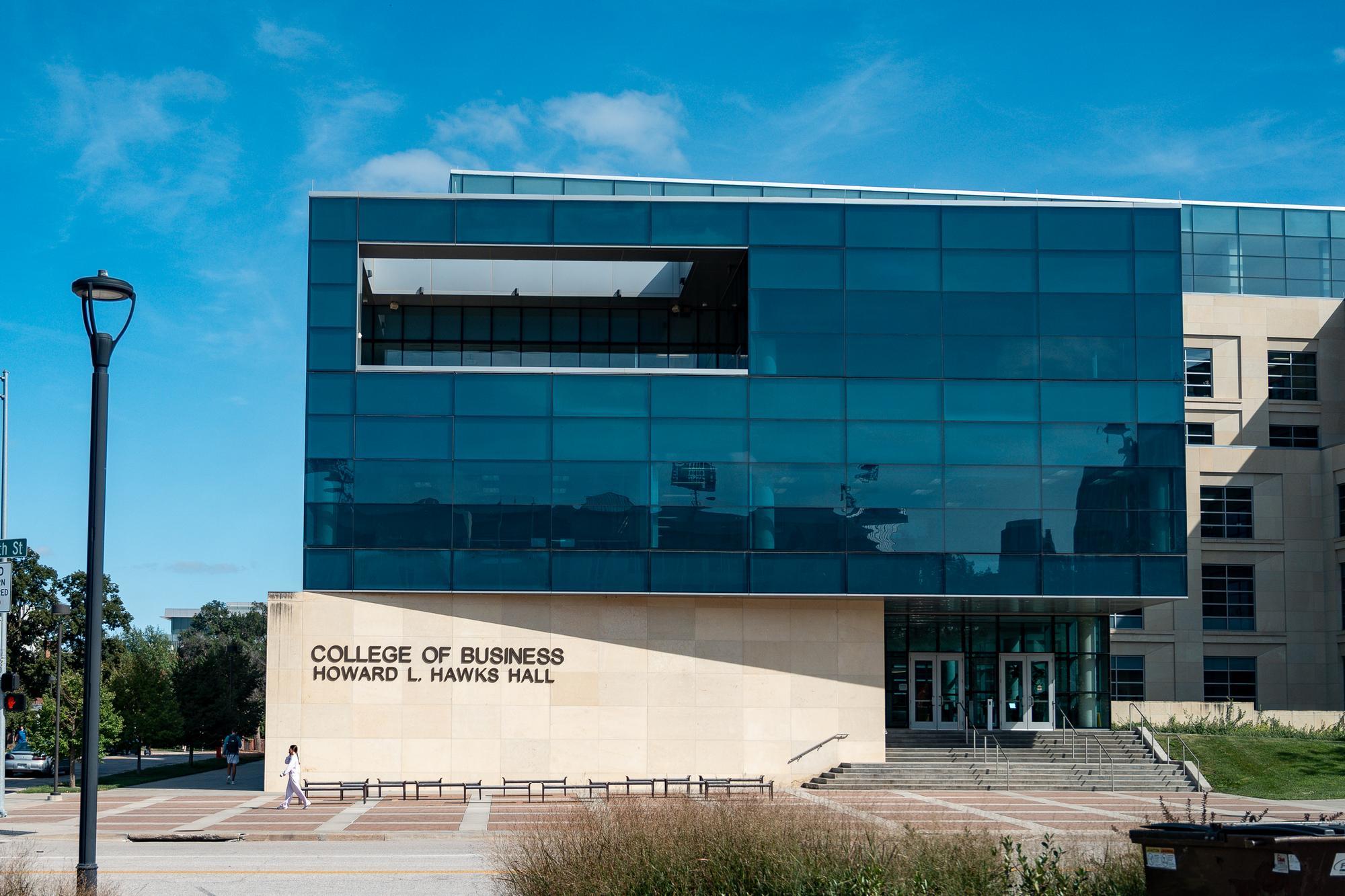 Howard L. Hawks Hall with glass exterior and beige stone walls, entrance visible under sunny sky.