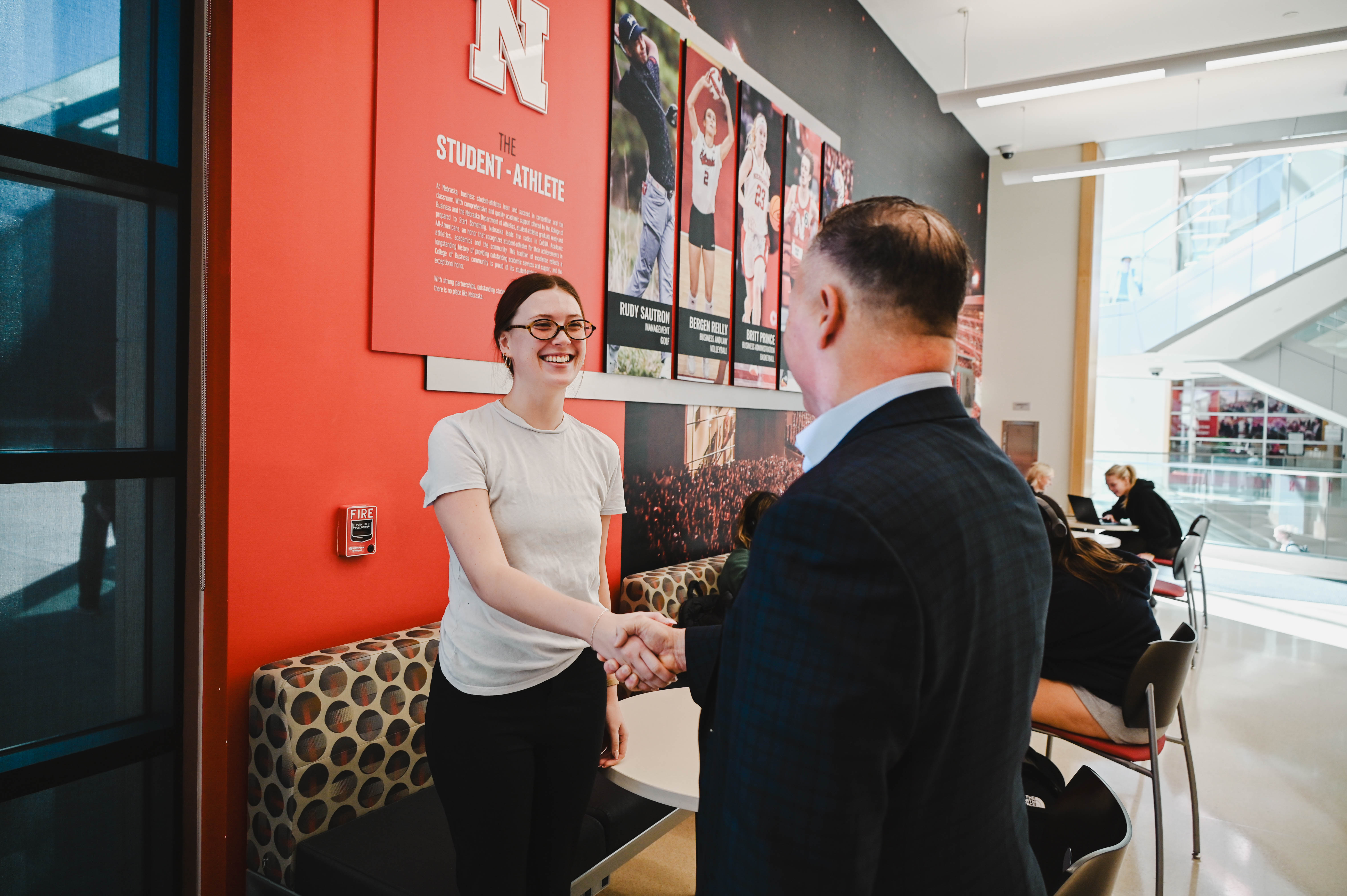 A man and woman shaking hands in a bright, modern indoor space.