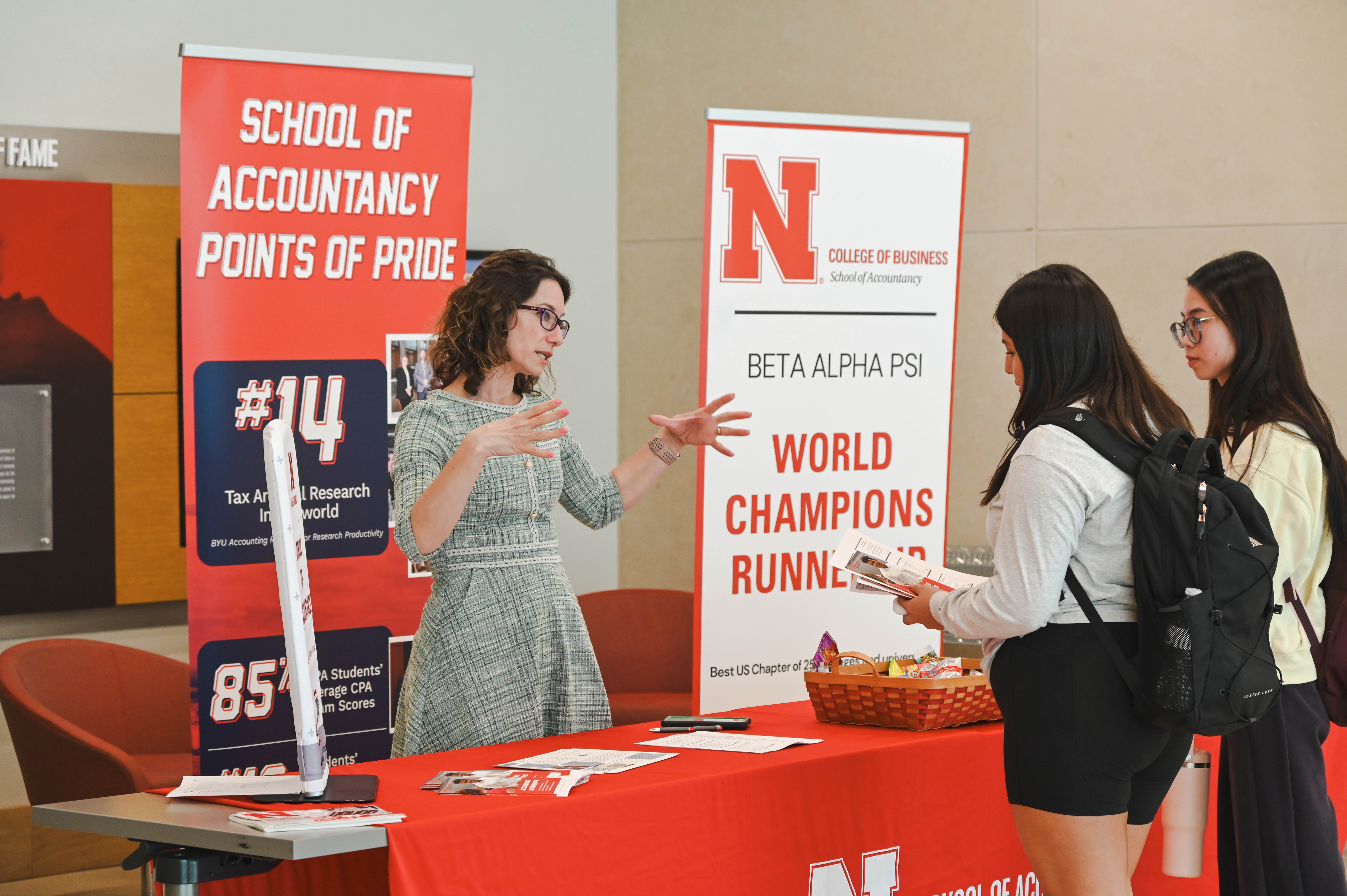 Person at a table interacting with students near business school banners.