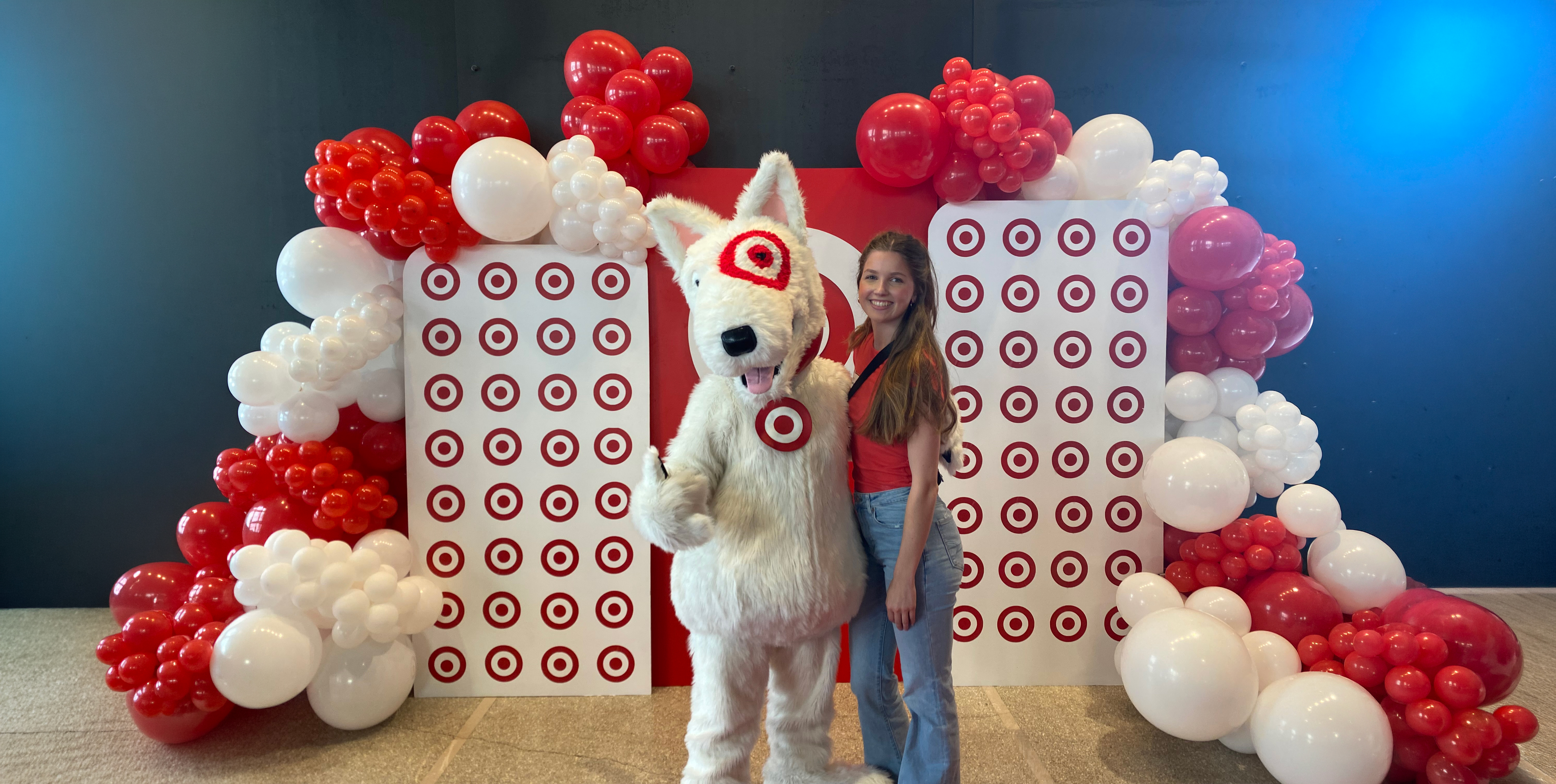 Person standing next to a Target mascot, surrounded by red and white balloon decorations.