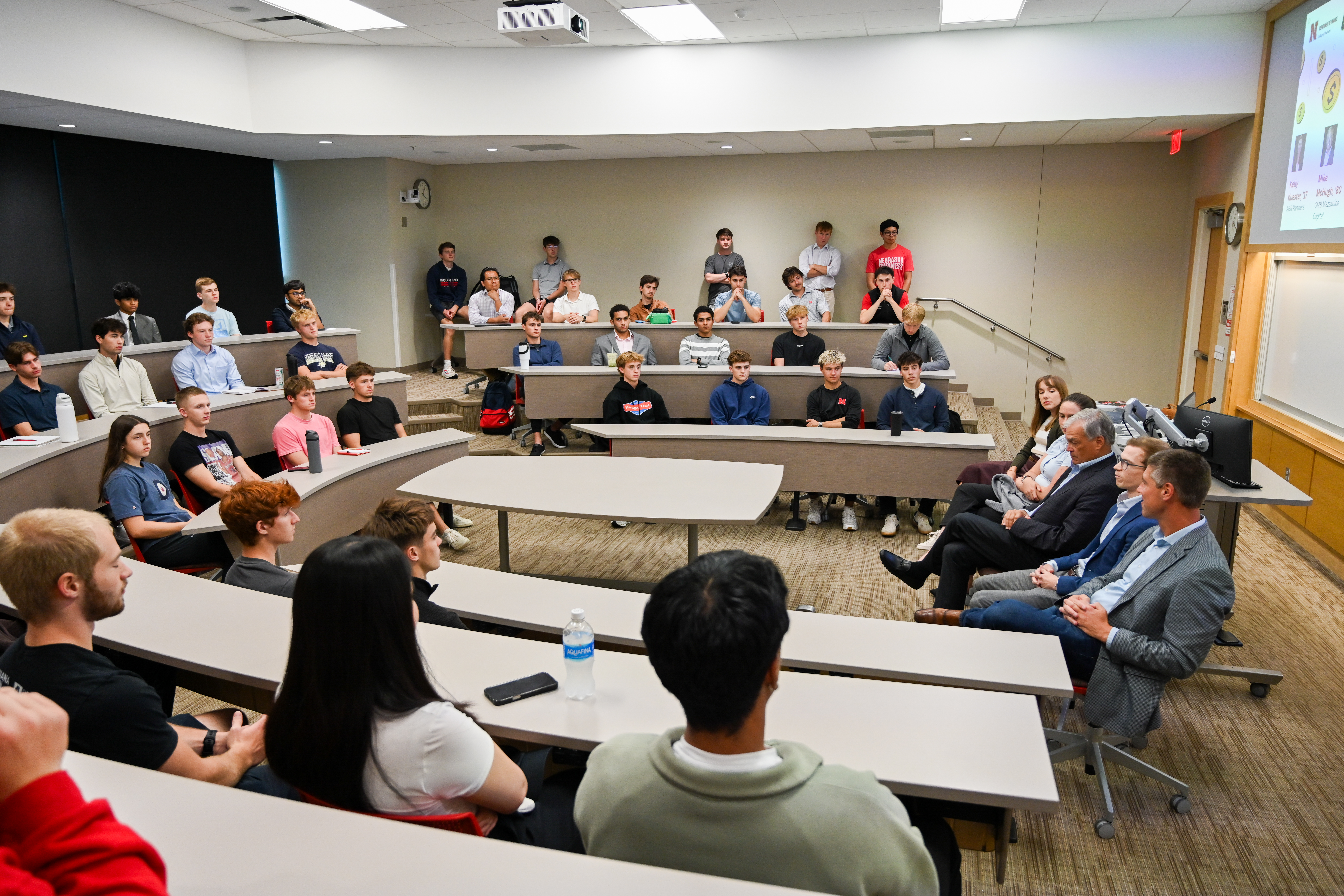 Audience in a lecture hall listens to a panel discussion moderated at the front of the room.