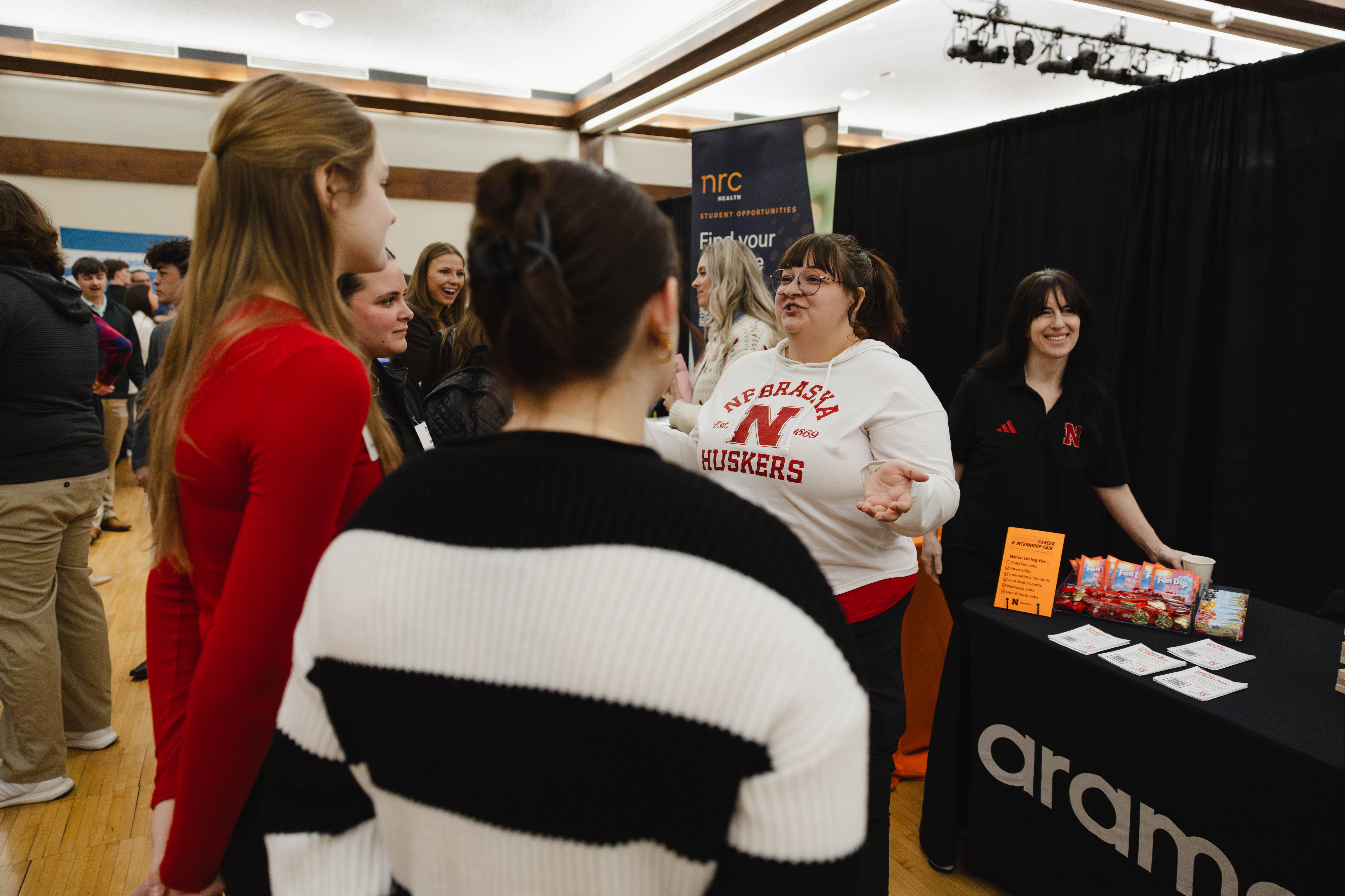 People interacting at a career fair, with a representative at a table displaying materials.