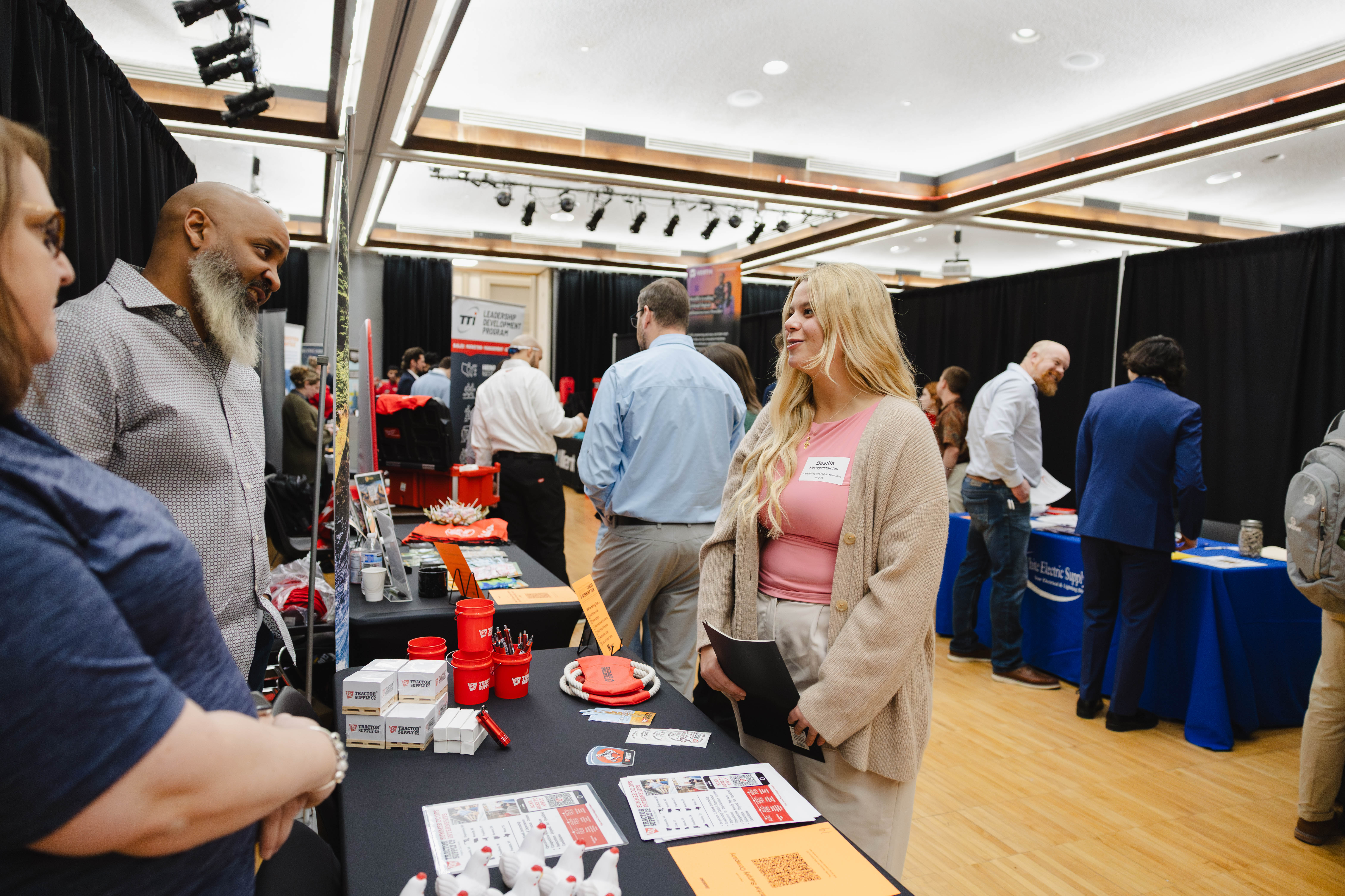 Booths and attendees at a career fair in a well-lit indoor venue.