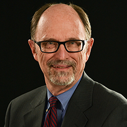 Man in suit and tie against a dark background, face blurred.