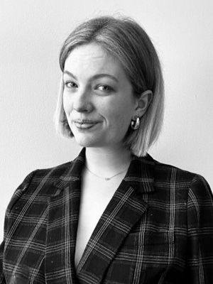 Smiling woman with short, light hair wearing a plaid blazer in a black-and-white photograph.