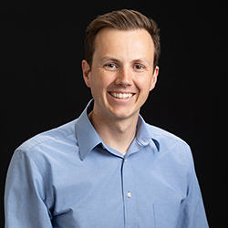 Man in a blue collared shirt against a black background.