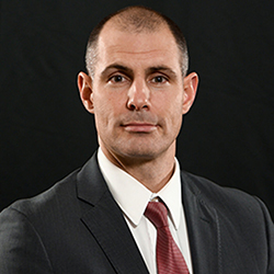 Man in a suit and tie against a black background, face blurred.