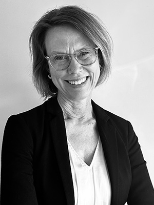 Smiling woman with glasses and short hair wearing a blazer and blouse, in black and white.