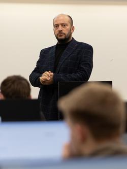 Man speaking in a classroom setting, with students seated in the foreground.