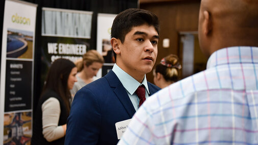 Male student at a career fair talking to a potential employer.