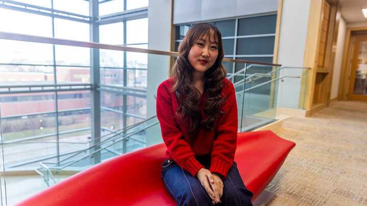 Emily sits on a red couch in Hawks Hall