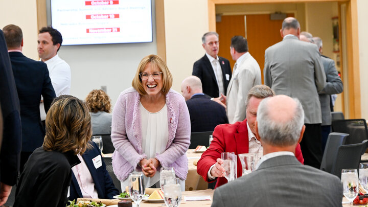 People seated and standing at a formal event with food and drinks on tables.
