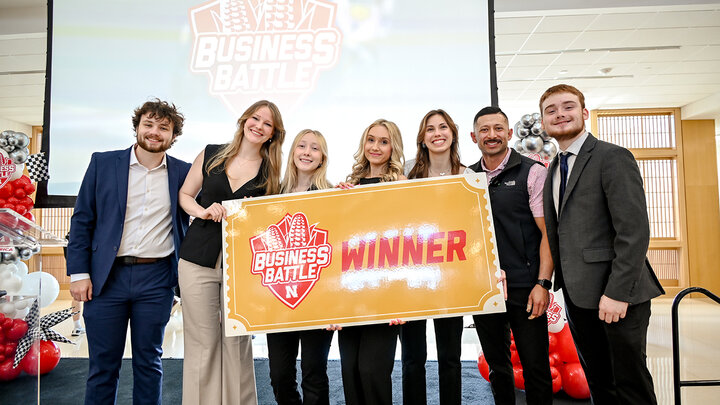 Business team holding a "Winner" sign at the Business Battle event; balloons in the background.
