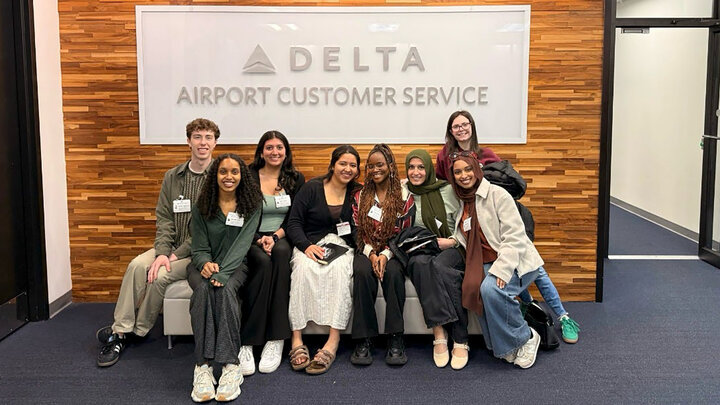 Students in professional attire sit in front of a sign that says Delta Airport Customer Service