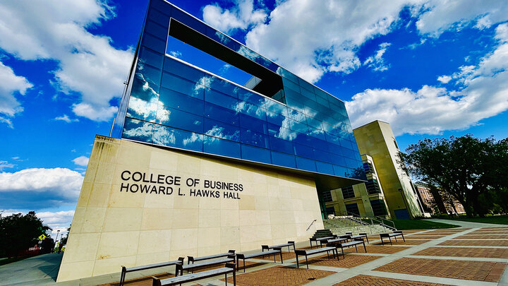 College of Business building with reflective glass, beige walls, benches, and a bright sky.
