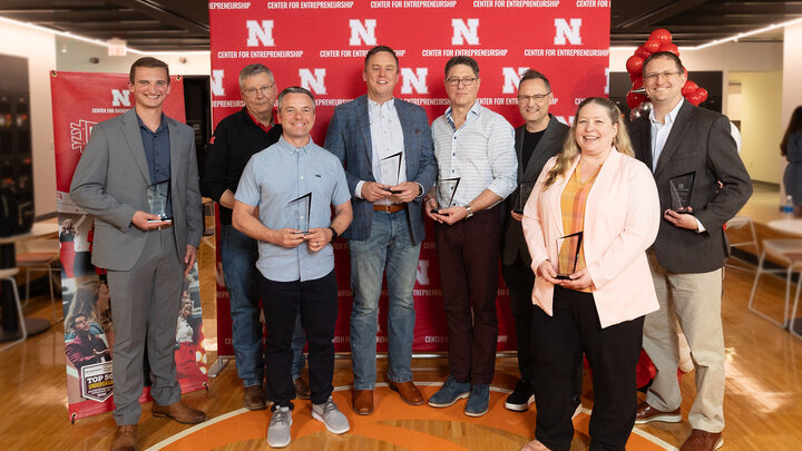 Group of people holding awards, standing on a wood floor, with a red "N" branded backdrop.