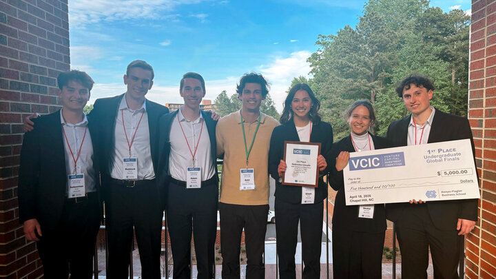 Seven people stand outdoors holding an award certificate and large prize check, dressed in business attire.