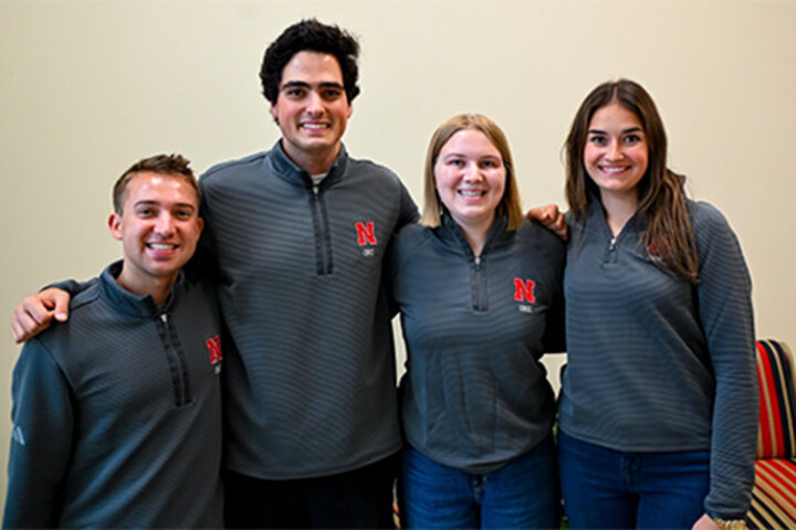 Four students in matching shirts with red N pose