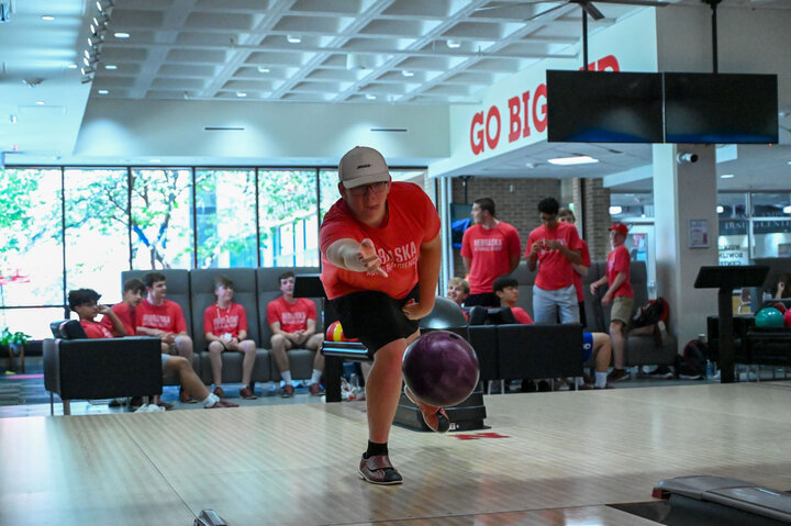 Male student rolls a bowling ball down the lane, toward the camera