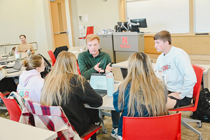 Alum Cade Crowell talks with four students in a classroom