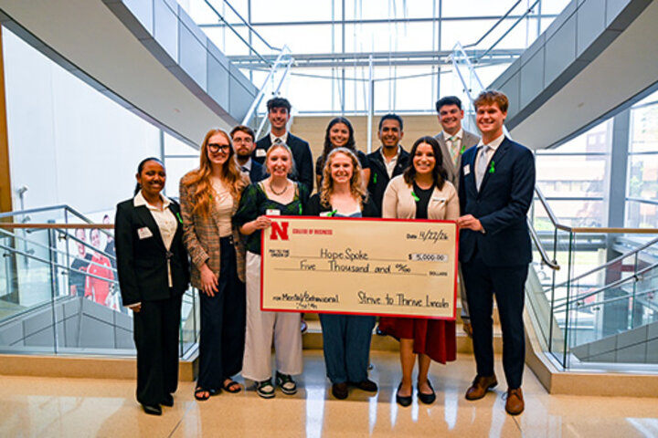Group standing in a bright atrium holding a large novelty check for $5,000.
