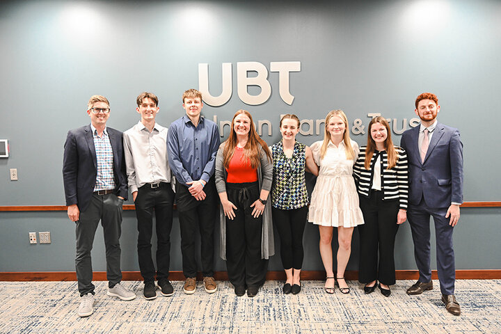 Group of people in formal attire standing in front of a wall with "UBT Union Bank &amp; Trust" logo.
